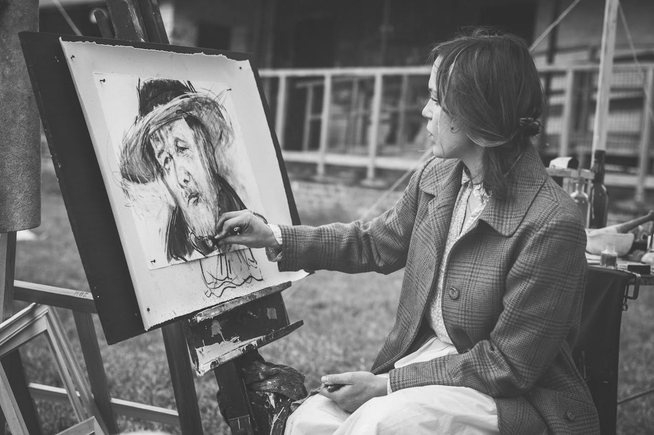 heros-img Woman painting a portrait outdoors in black and white.