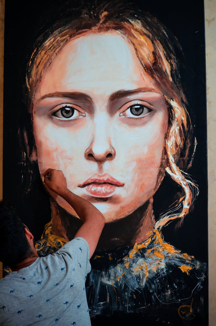 about-us-02 An artist meticulously paints a large portrait of a woman on canvas in an indoor art studio.